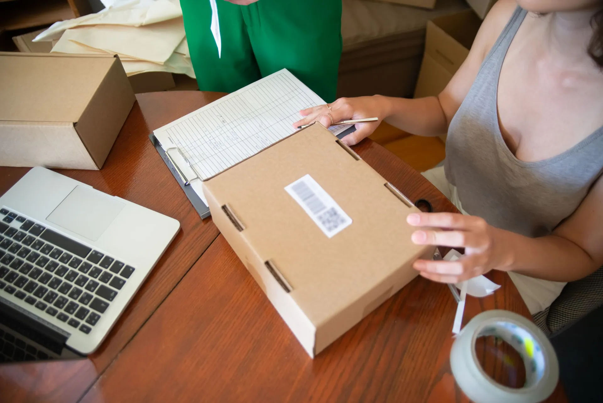 Packing an order against a picklist, with a barcoded box, laptop and tape on the bench